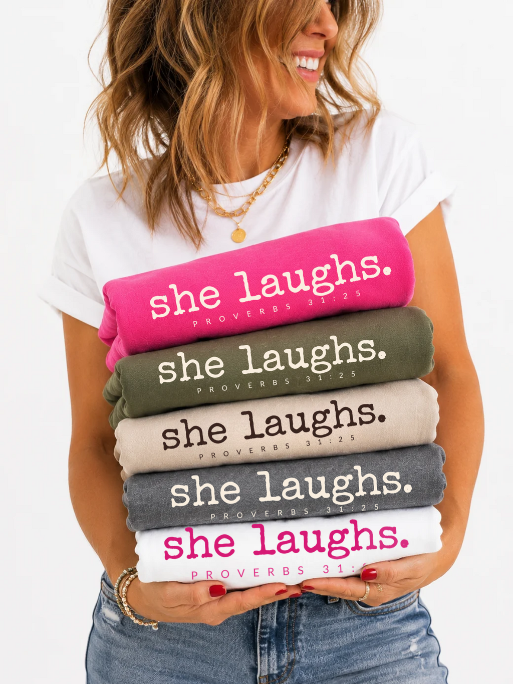 Woman holding folded She Laughs Proverbs 31:25 sweatshirts in five colors