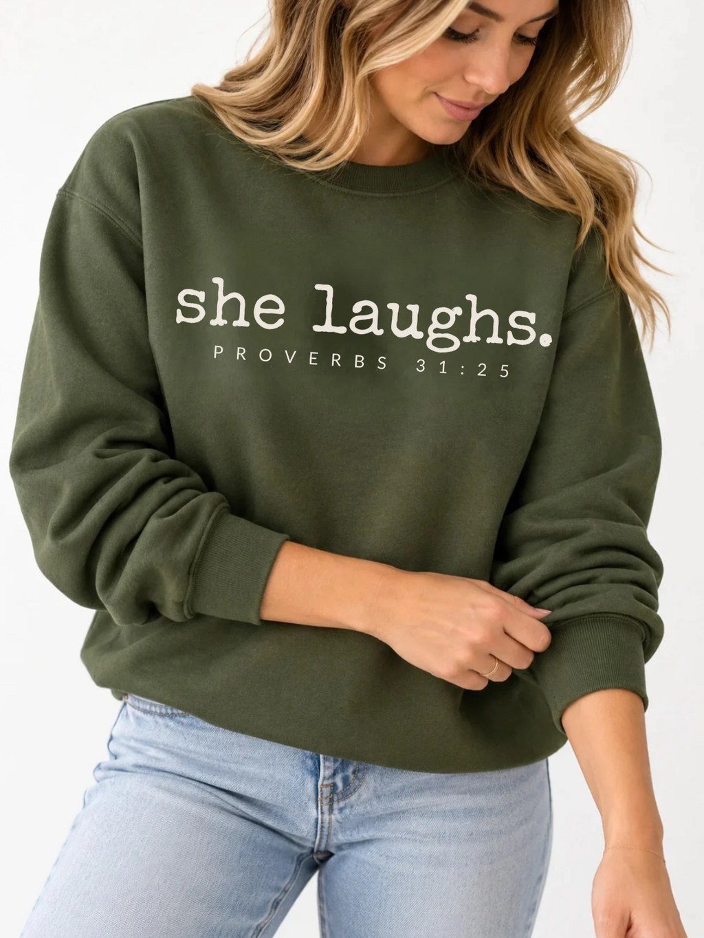 Woman wearing a military green She Laughs sweatshirt with ivory Proverbs 31:25 lettering