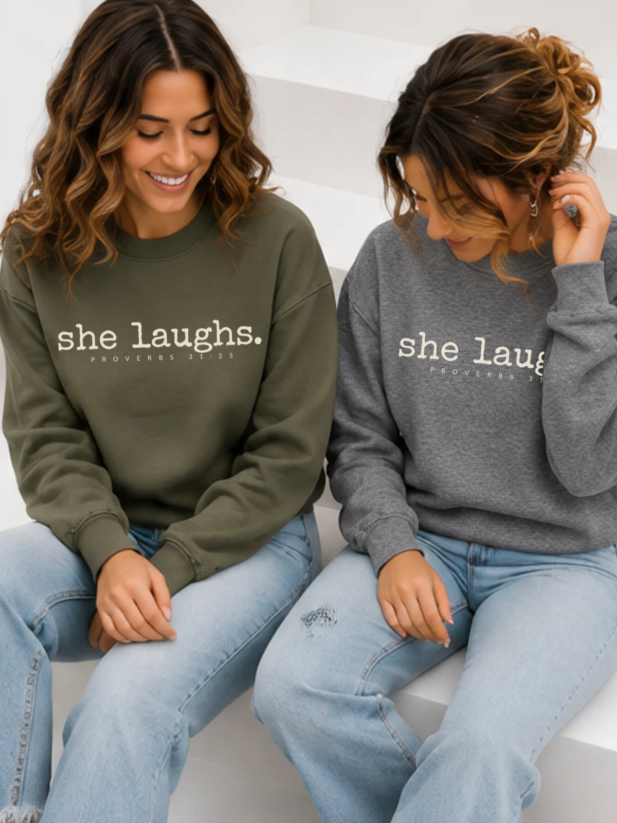 Two women wearing military green and gray She Laughs sweatshirts