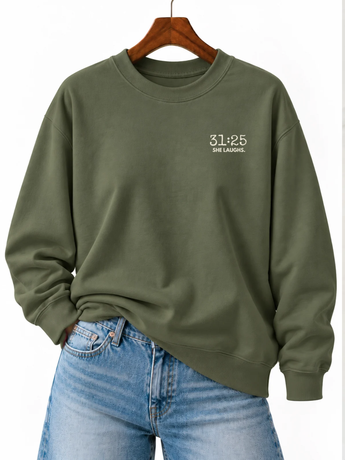 Military Green 31:25 Minimal Sweatshirt with small ivory left-chest print, displayed on a wooden hanger and styled with blue jeans.