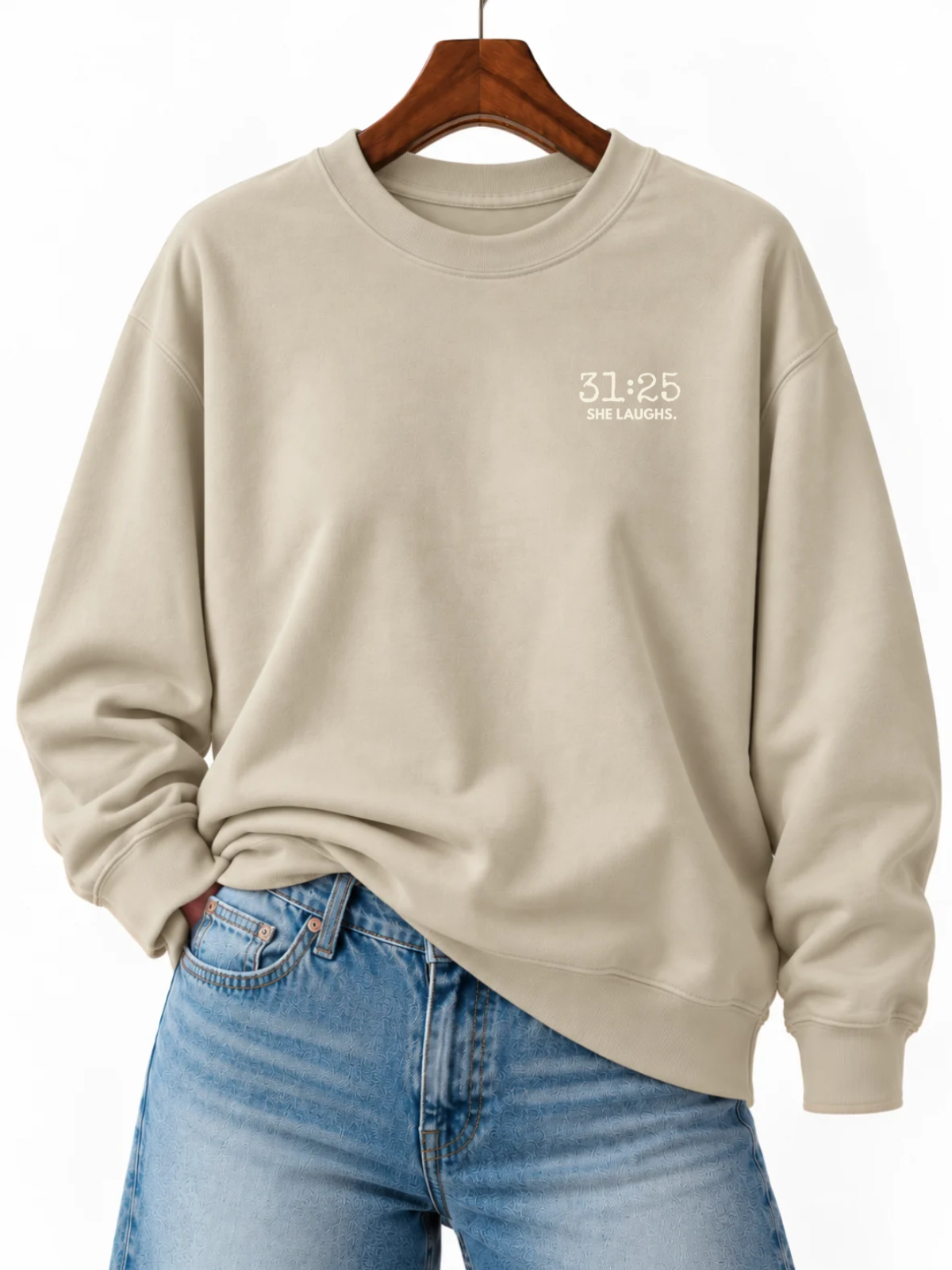 Sand 31:25 Minimal Sweatshirt with small ivory left-chest print, displayed on a wooden hanger and styled with blue jeans.