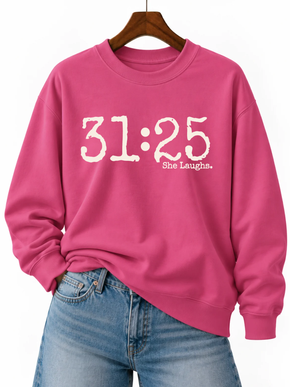Heliconia pink 31:25 sweatshirt with oversized ivory front lettering, styled on a wooden hanger with blue jeans.