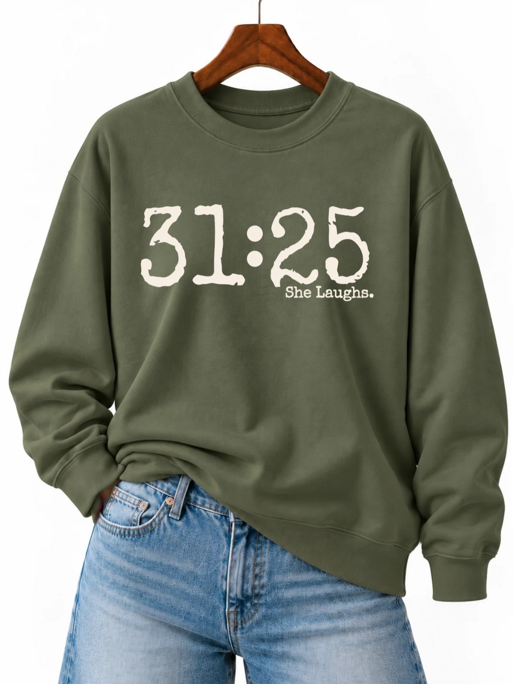 Military Green 31:25 sweatshirt with large ivory front print, displayed on a wooden hanger with blue jeans.