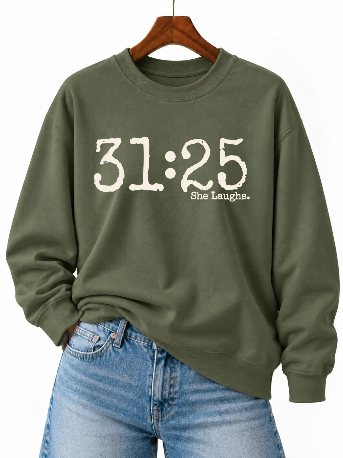 Military Green 31:25 sweatshirt with large ivory front print, displayed on a wooden hanger with blue jeans.