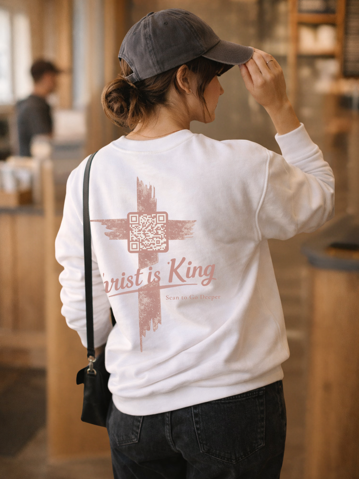 woman wearing a white sweatshirt with a cross and John 12:12-15 on back in a coffee shop