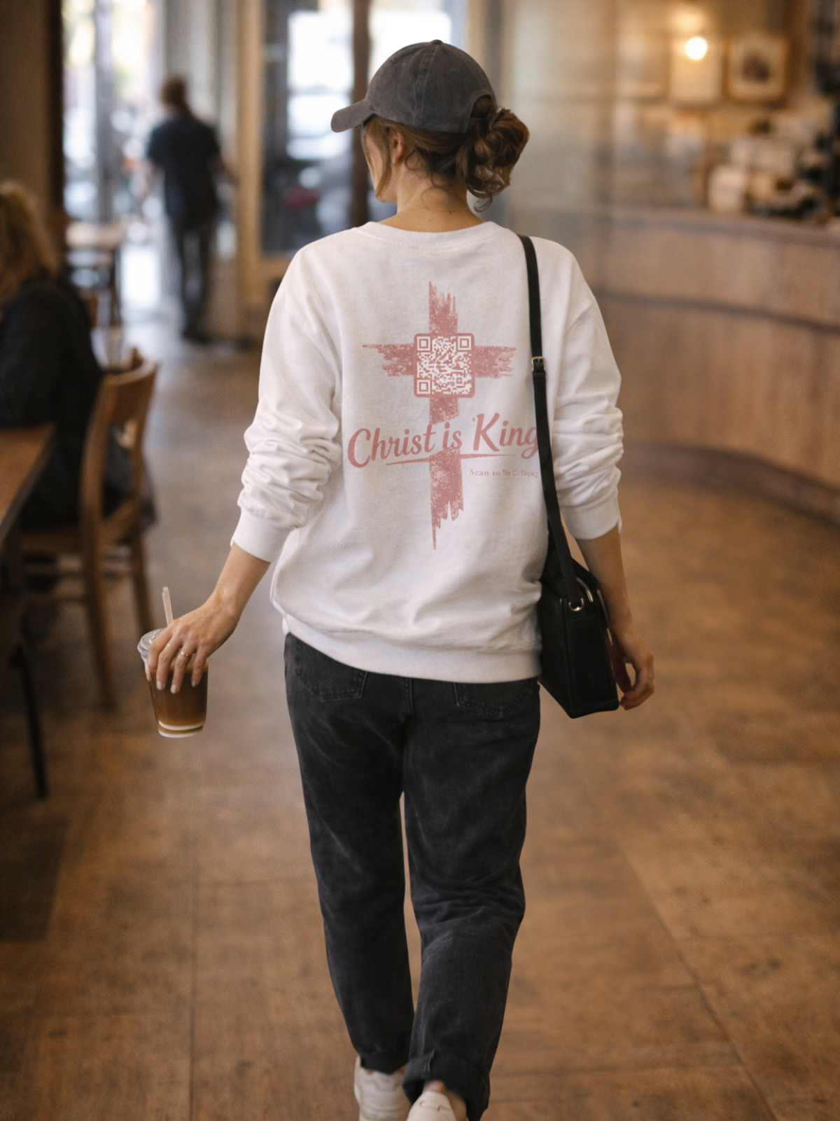 Woman wearing a white sweatshirt with 'Christ is King' text walking in a cafe. John 12:12-15