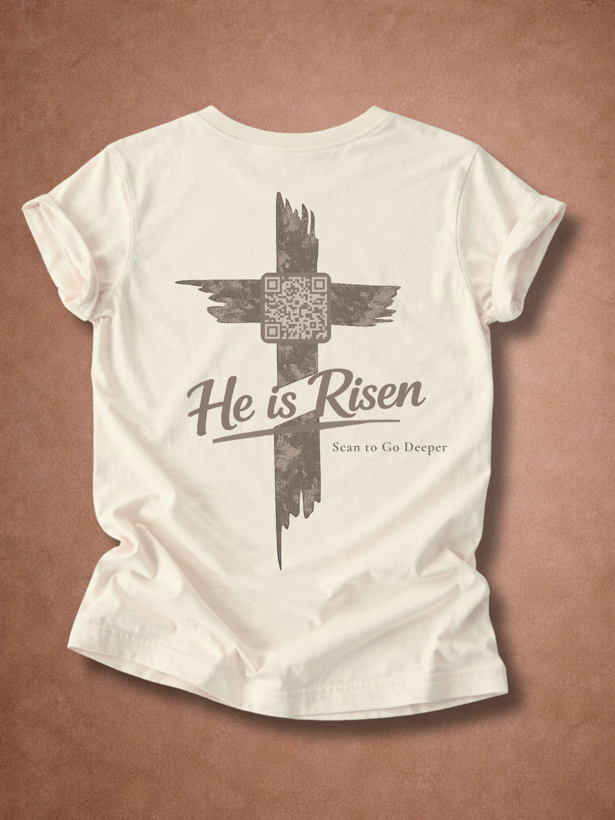 Natural t-shirt with a cross design and 'He is Risen' text on a brown background