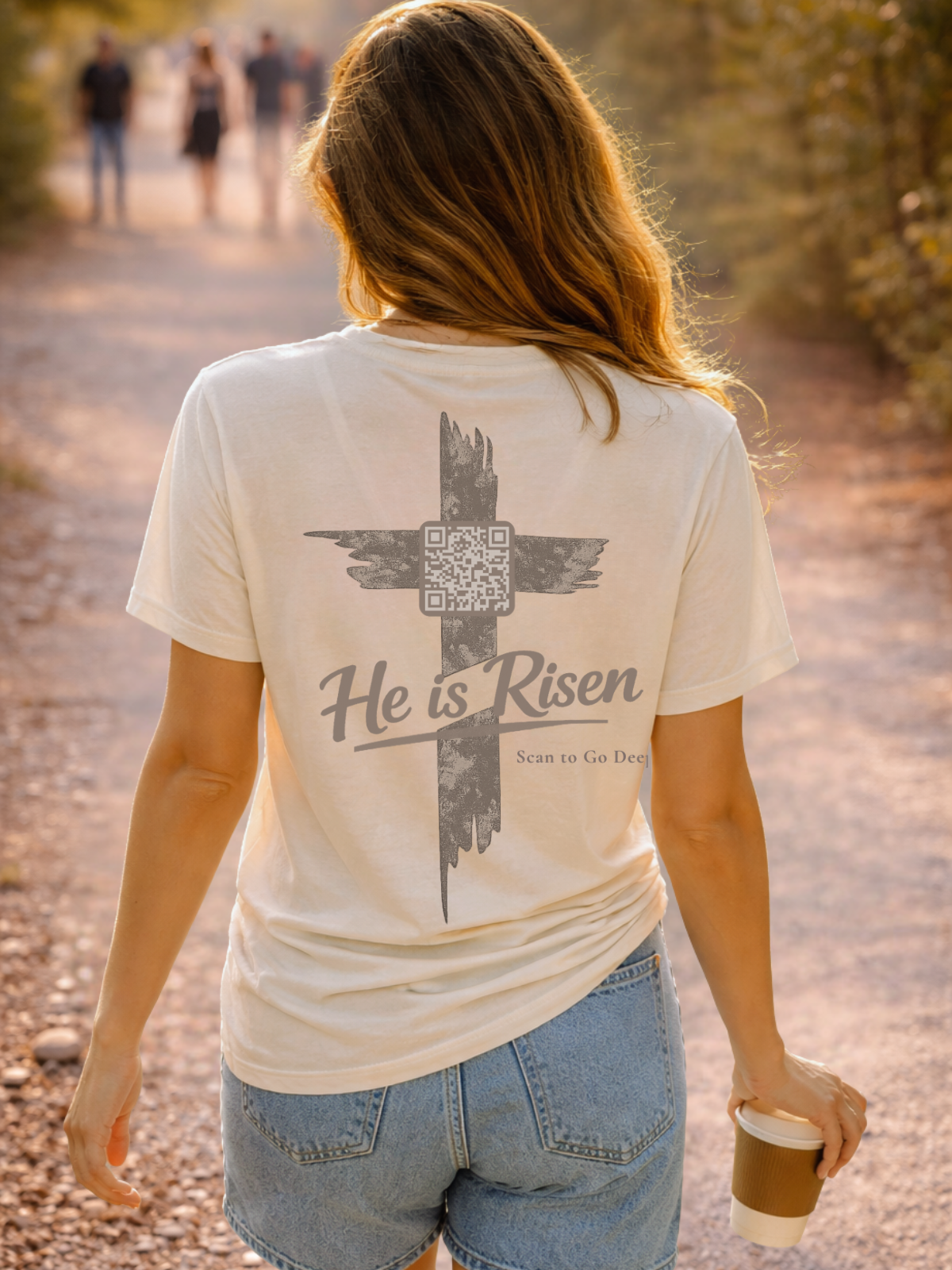Person wearing a t-shirt with 'He is Risen' design and QR code, walking outdoors.