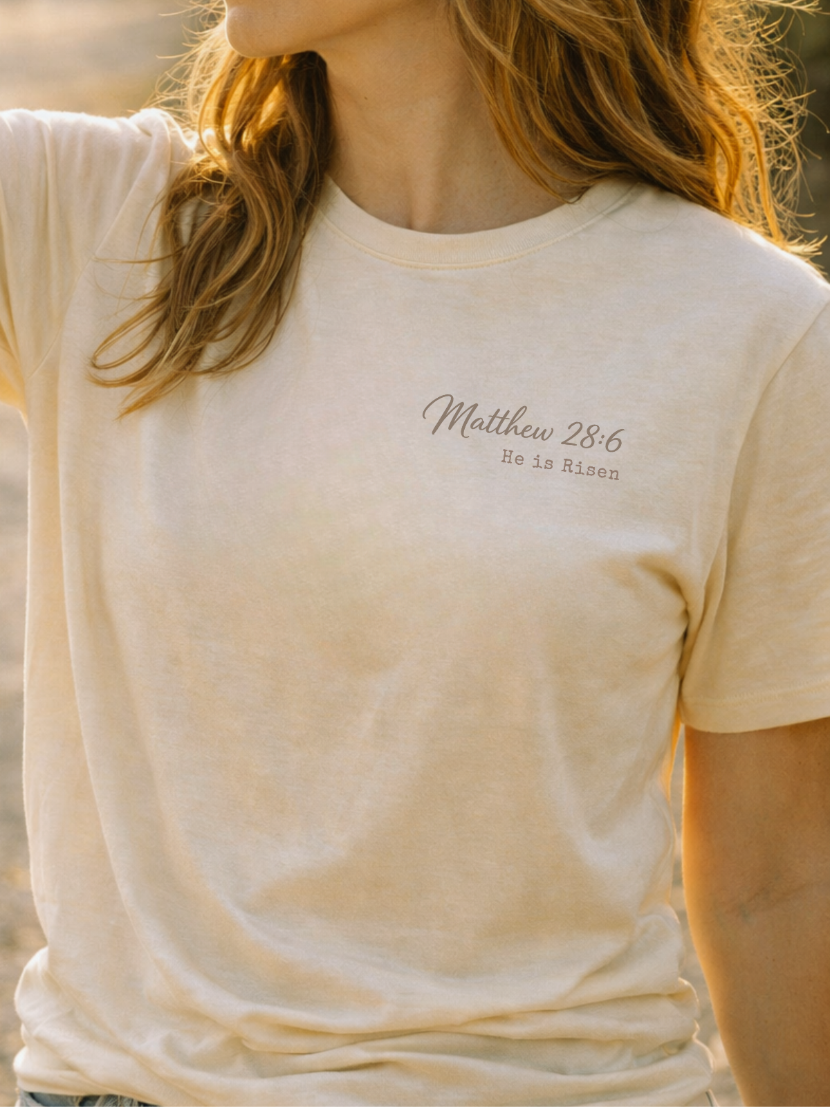 Person wearing a beige t-shirt with 'Matthew 28:6 He is risen' text.