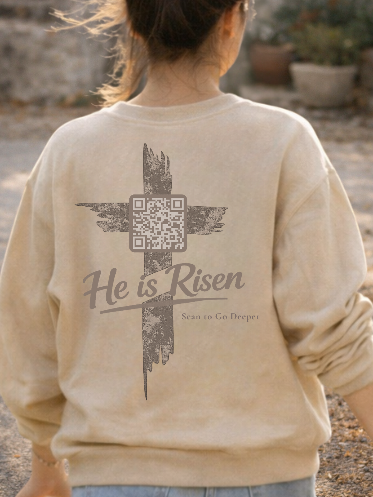 Beige sweatshirt with 'He is Risen' text and QR code on the back, worn by a Christian Woman outdoors. Matthew 28:6
