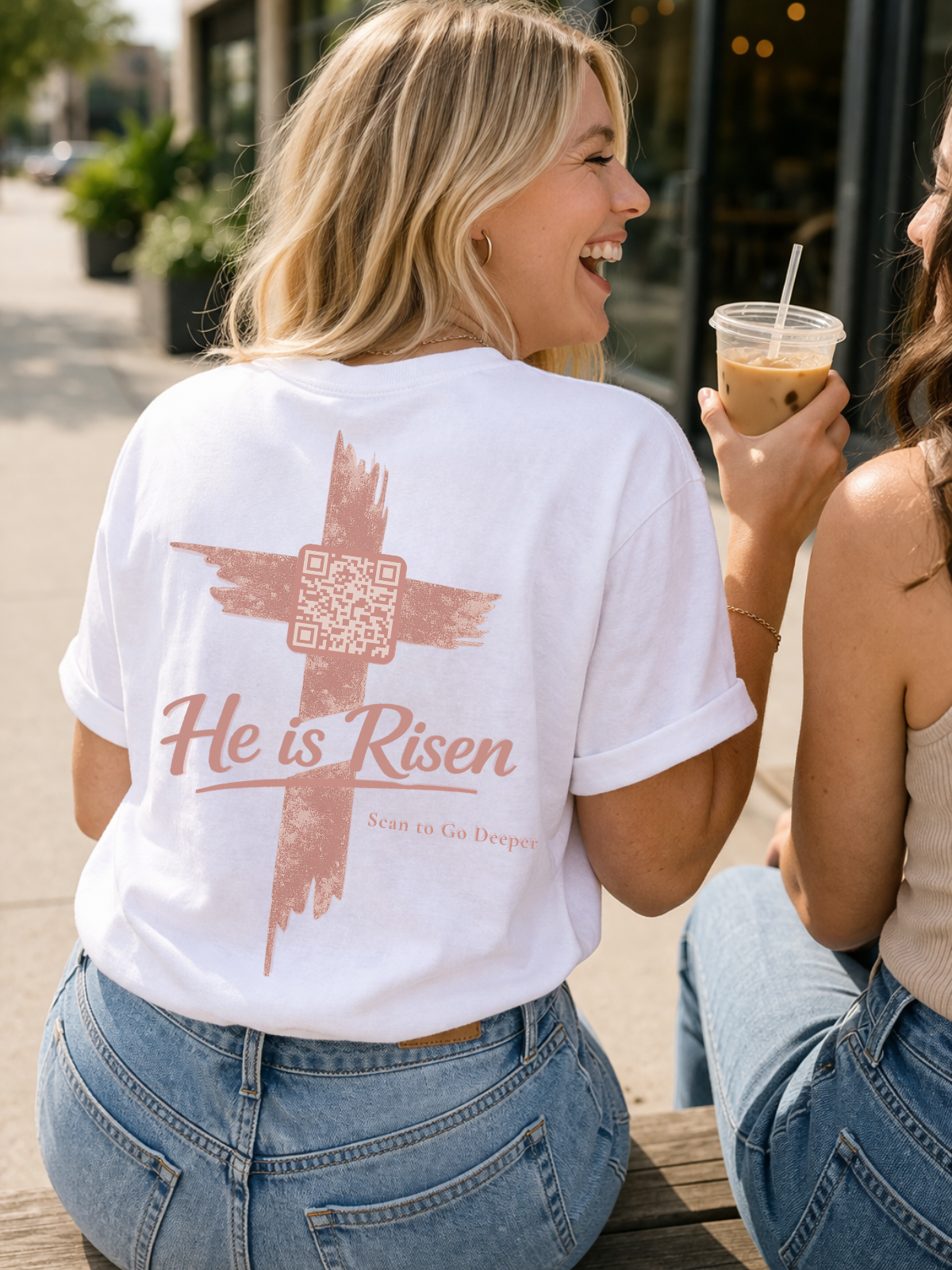 Woman wearing a white t-shirt with a cross and 'He is Risen' text, sitting outdoors.