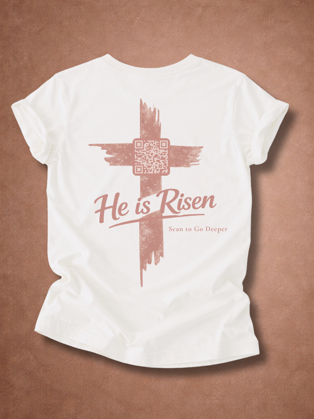 White t-shirt with a cross and 'He is Risen' text on a brown background